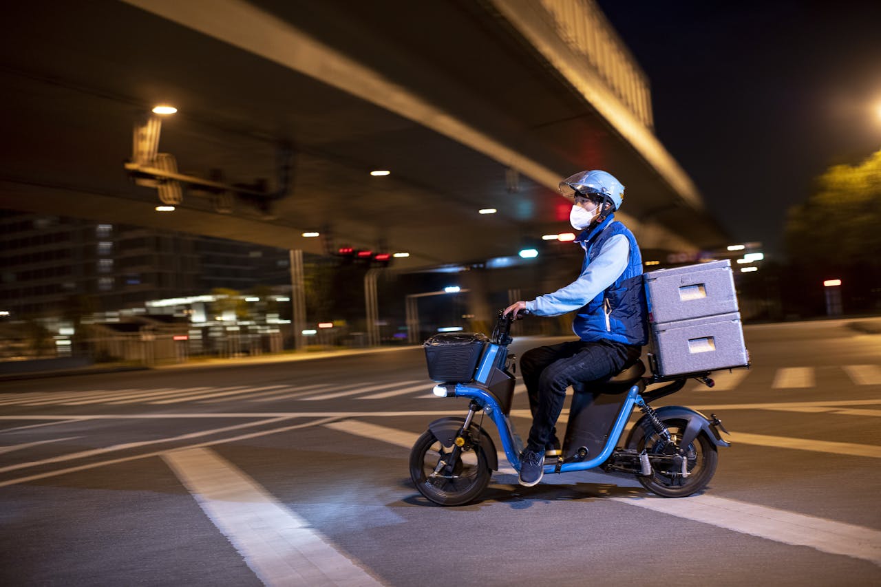 A masked delivery driver rides an electric scooter on Wuhan city streets at night.